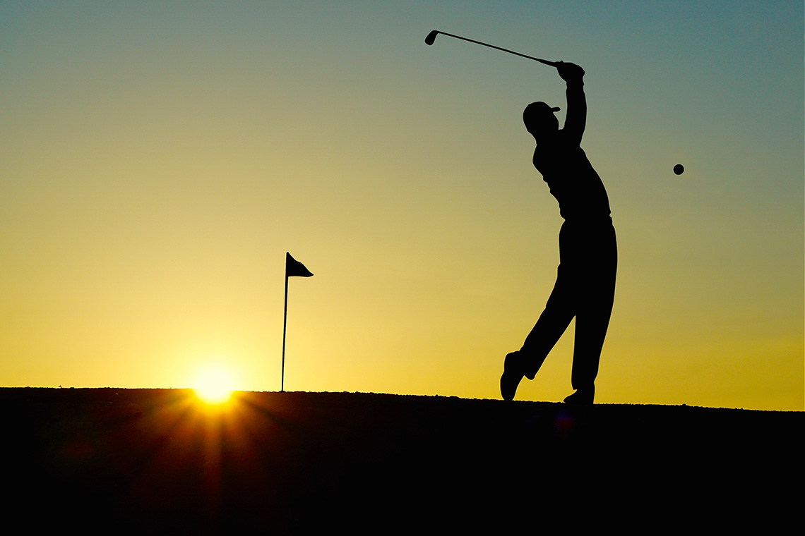 Golfer following through during sunset